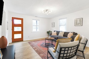 A living room with a sofa, coffee table, and a rug. There are two windows and a door.