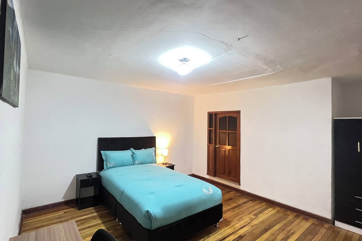 A bedroom with a bed, a nightstand, a lamp, a wooden door, and a wardrobe.