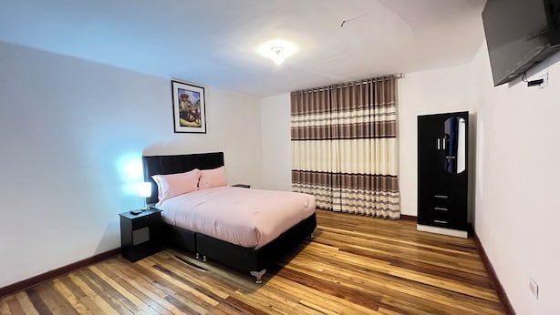 Un dormitorio con cama, mesita de noche y televisor instalado en la pared.