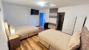 Un dormitorio con dos camas, un televisor montado en la pared, un armario y una puerta que da al baño.