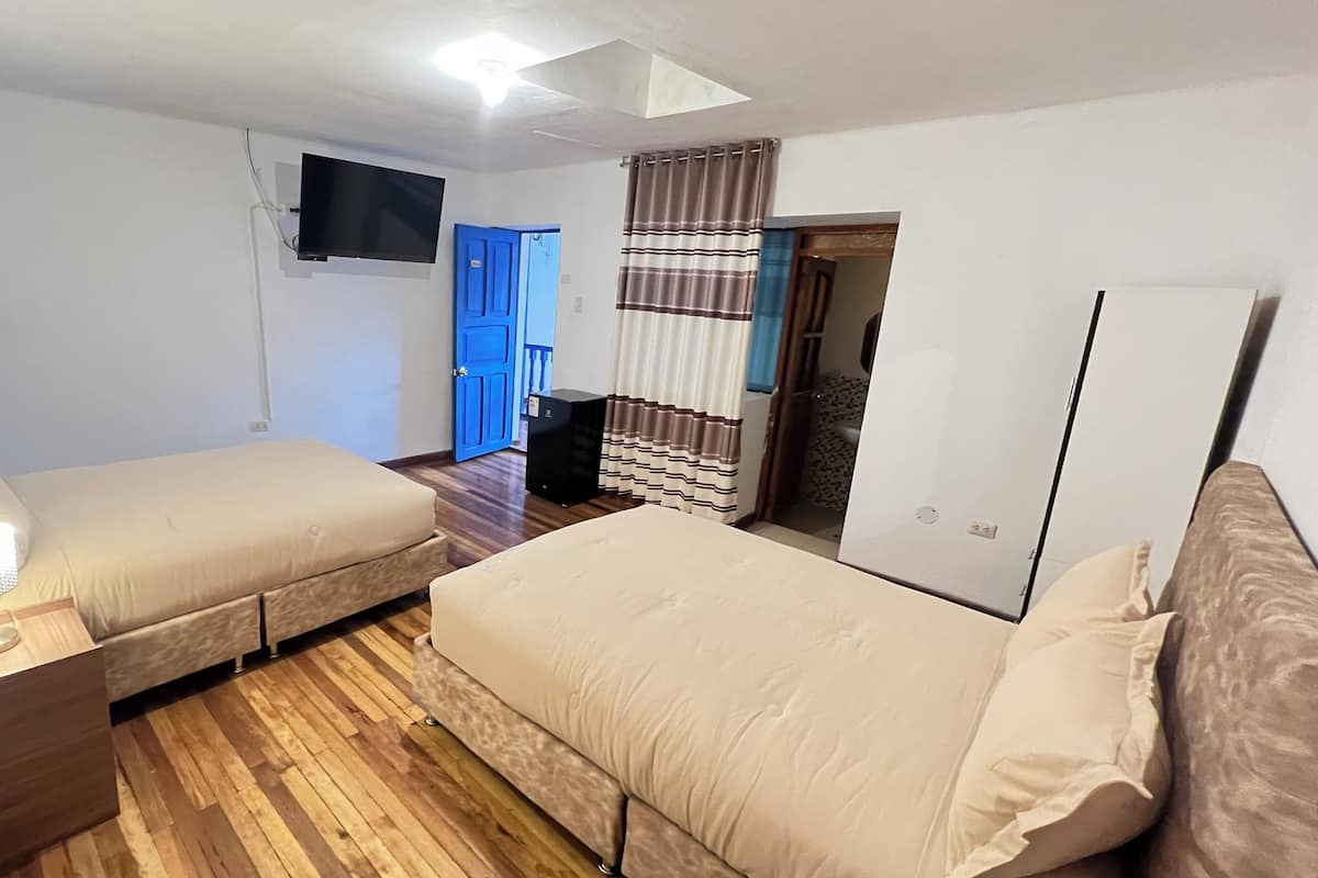 A bedroom with two beds, a TV mounted on the wall, a wardrobe, and a door leading to a bathroom.