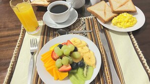 Desayuno con tostadas, huevos revueltos y una bandeja de fruta.