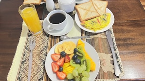 Un desayuno con una fuente de fruta, tostadas, café y zumo de naranja sobre una mesa.