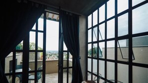 Una habitación con ventanas amplias, un balcón con sillas y vistas a la ciudad.