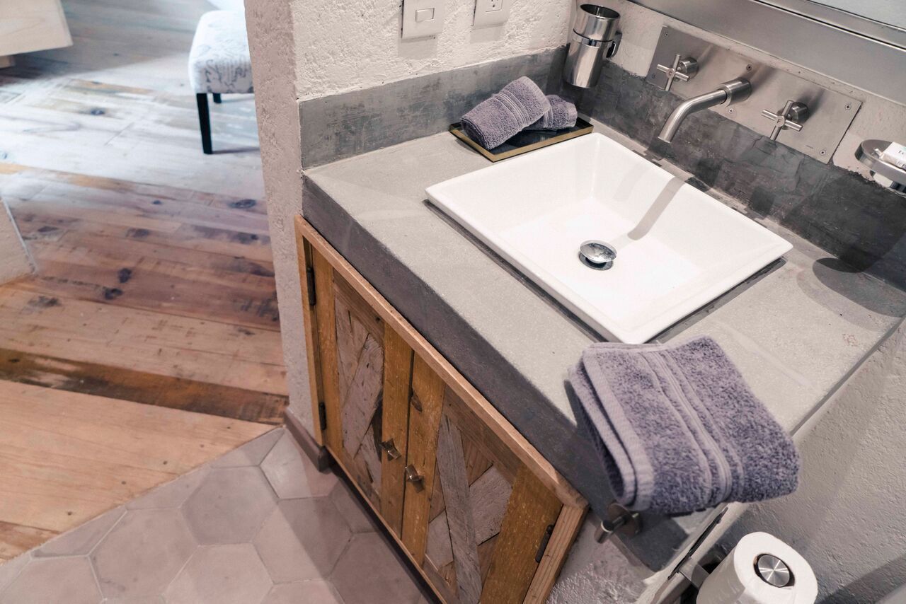 Un baño con lavamanos blanco, mueble de madera y un perchero para toallas.
