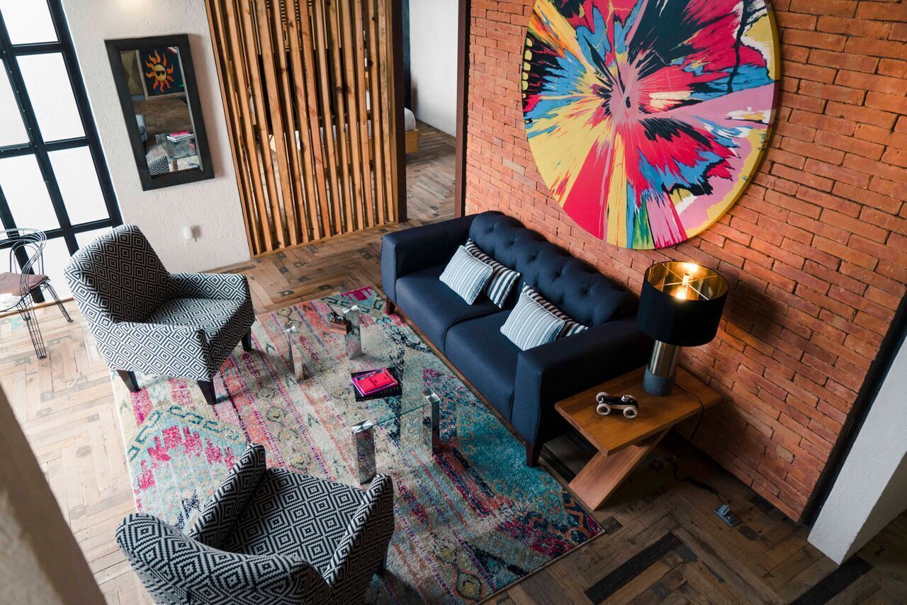 Un salon moderne avec un canapé noir, des fauteuils à motifs, une peinture abstraite aux couleurs vives et une table basse en bois.