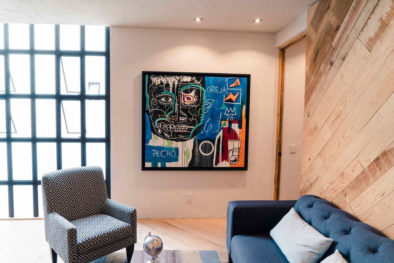 Un salon moderne avec un fauteuil à motifs géométriques, un canapé bleu foncé et un grand tableau abstrait accroché au mur.