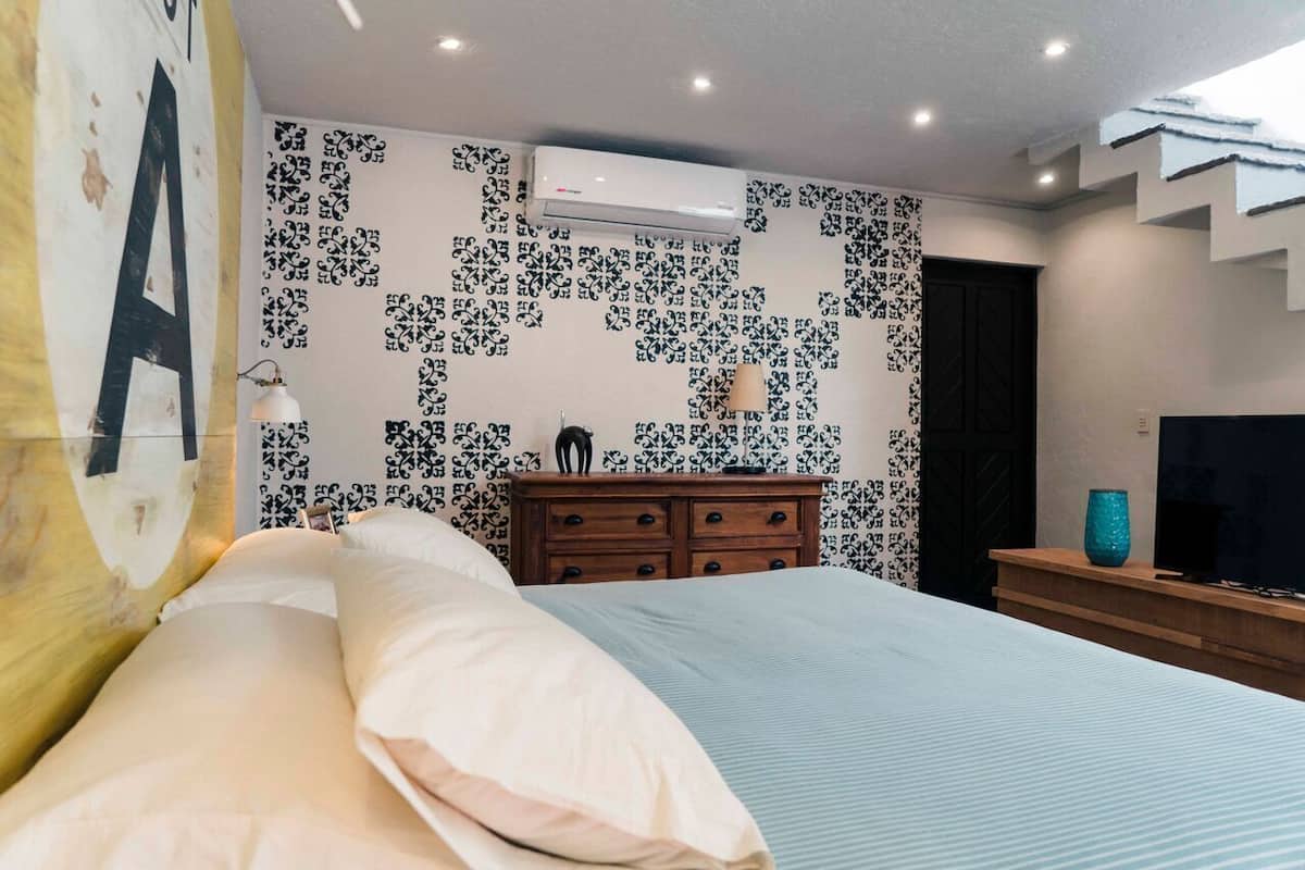 A modern bedroom with a bed, dresser, and wall-mounted air conditioner.