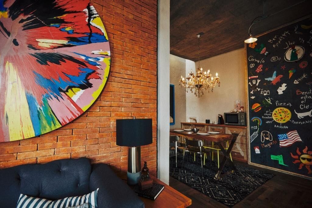 A modern living room with a large abstract painting, a chandelier, and a dining area visible through an open door.