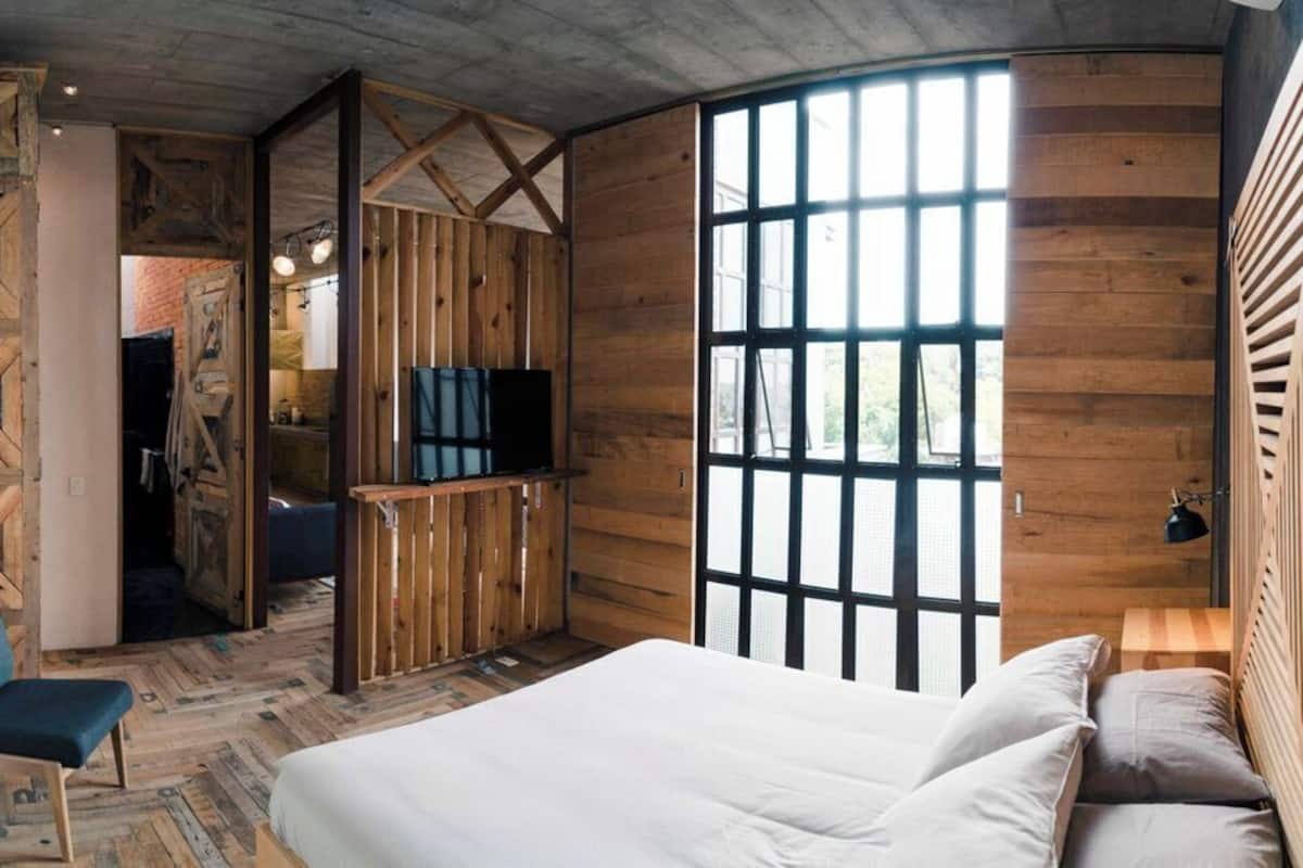A bedroom with a large bed, a chair, a TV, and a window.