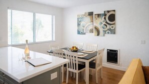 Una cucina moderna con zona pranzo, mobili bianchi, forno integrato e finestra con persiane.