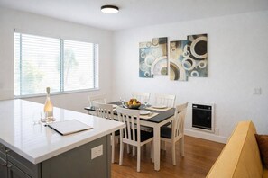 A modern kitchen with a dining area, white cabinetry, a built-in oven, and a window with blinds.