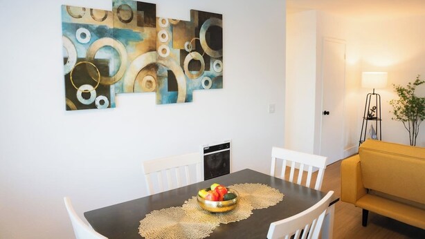A dining area with a table set for two, a fruit bowl on the table, and a modern abstract painting on the wall. - Guest Favorite! Easy Walk to Beach - Food & Shops! (Oceanside)