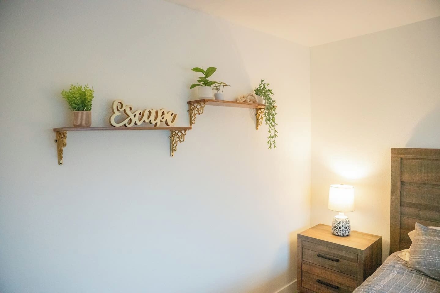 A bedroom with a bed, a nightstand with a lamp, and two wall-mounted shelves with plants and decorative items.