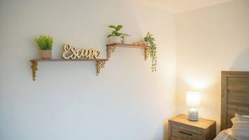 A bedroom with a bed, a nightstand with a lamp, and two wall-mounted shelves with plants and decorative items.