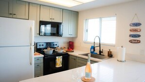 A modern kitchen with white countertops, a black stove, and a microwave. There is a window with blinds, a sink, and a decorative sign on the wall. - Guest Favorite! Easy Walk to Beach - Food & Shops! (Oceanside)