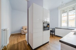 Et moderne køkken med hvide skabe, ovn og et vindue med udsigt til bygninger.