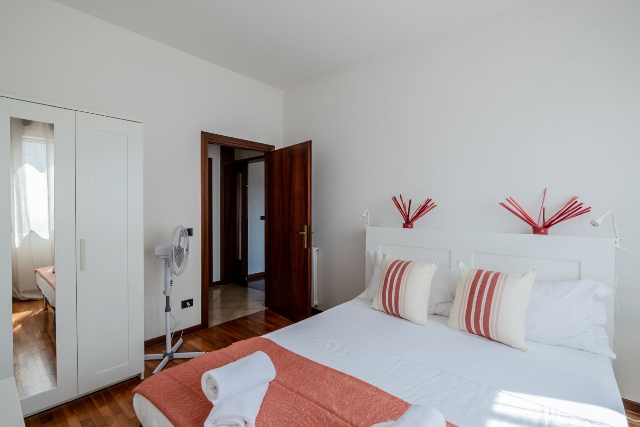 A bedroom with a bed, a fan, a wardrobe, and a door leading to another room.