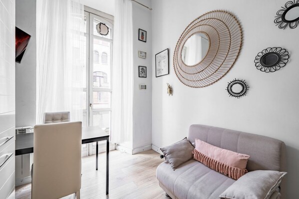 A modern living room with a sofa, a dining table, and a chair. There are wall decorations and a large mirror.