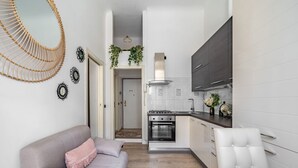 Une cuisine moderne avec des meubles blancs, une cuisinière et un four à micro-ondes. On y trouve un coin repas avec une table et des chaises, ainsi qu’un salon avec un canapé et des œuvres d’art décoratives au mur.