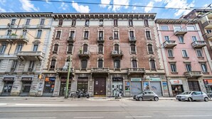 Un immeuble à plusieurs étages, doté d’une entrée centrale, de plusieurs fenêtres et donnant sur une rue.