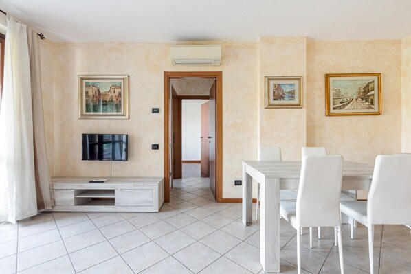 Une piĂšce Ă©quipĂ©e dâun tĂ©lĂ©viseur, dâune table Ă manger, de chaises et de tableaux aux murs.