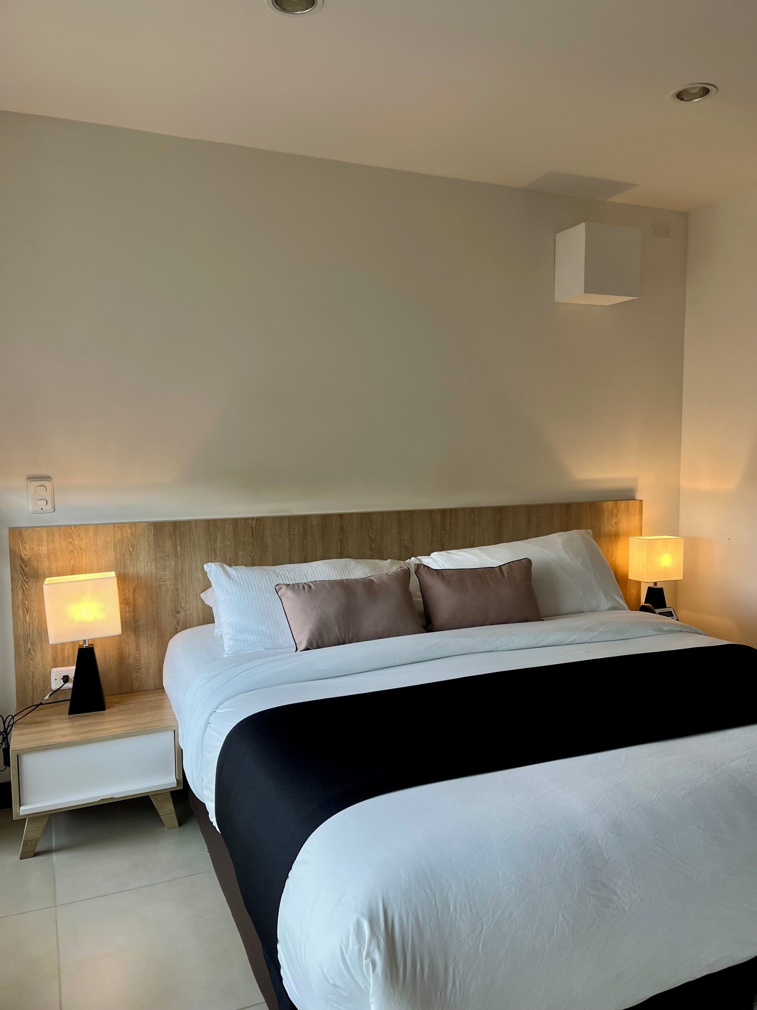 Habitación de hotel con una cama grande, dos mesitas de noche y dos lámparas de pared.