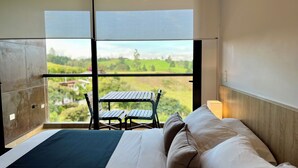 A bedroom with a large window, a bed, and a small table with chairs. - Hotel Rioverde- 5 minutos de cercanía al aeropuerto (Rionegro)