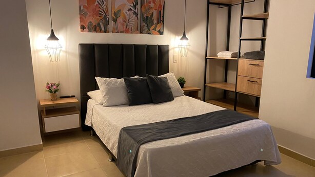 Un dormitorio ordenado con cama, mesitas de noche, estante en la pared y lámpara colgante.