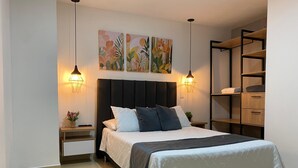 A neatly arranged bedroom with a bed, bedside tables, a nightstand, a wall-mounted shelf, and two wall-mounted lamps. - Praia Apartaestudios (Sabaneta)