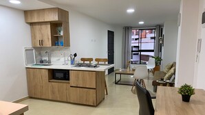 Una cocina moderna con armarios de madera, microondas integrado y estufa a gas. Hay un comedor con mesa y sillas, y vistas al exterior a través de amplias ventanas.