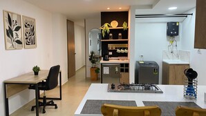 A modern kitchen with a gas stove, sink, and a built-in oven. There is a dining area with a table and chairs, and a small office space with a desk and chair. - Praia Apartaestudios (Sabaneta)