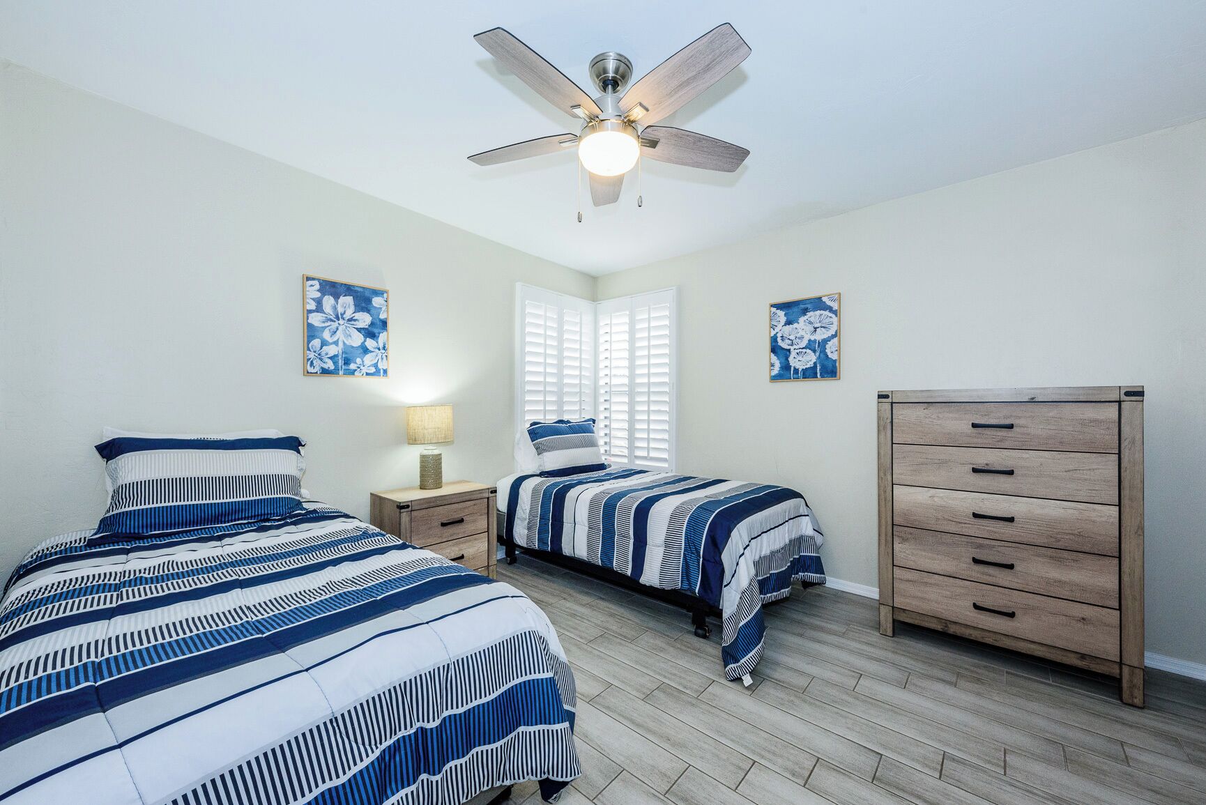 Une chambre avec deux lits, un ventilateur de plafond, une commode et deux lampes fixées au mur.