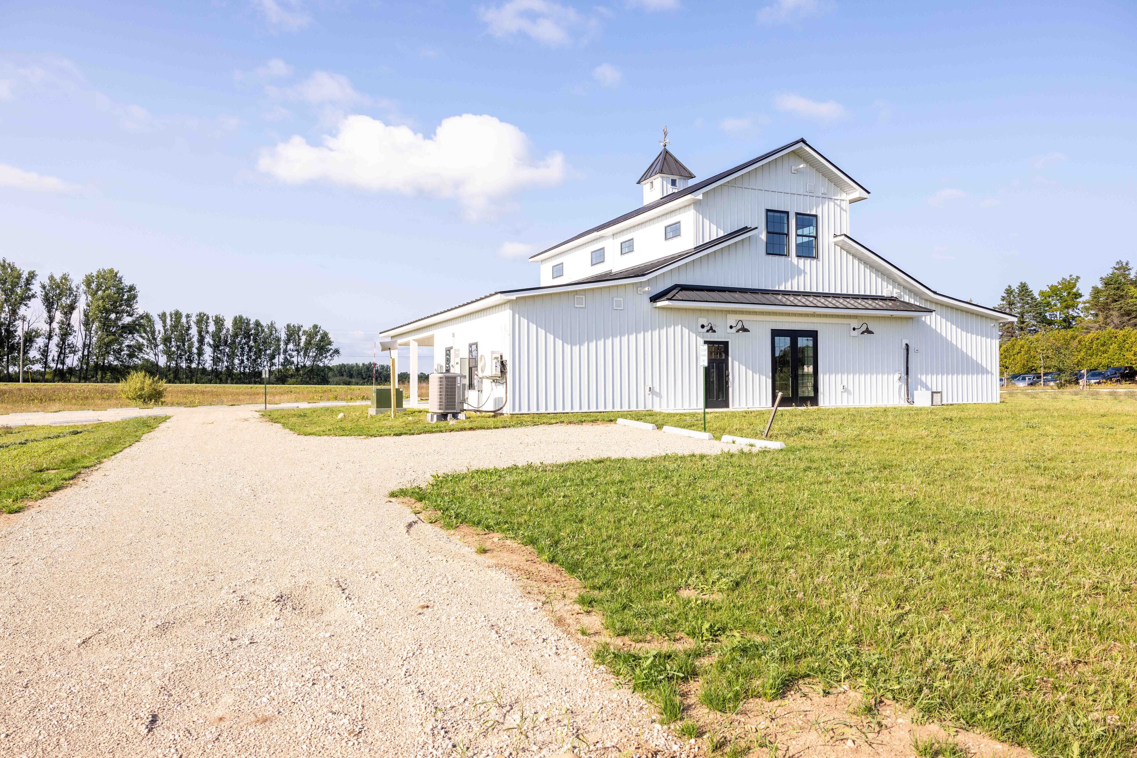 A white building with a central door and windows, surrounded by a gravel path and grassy area.