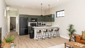 A modern kitchen with dark green cabinets, a black refrigerator, and a white island with bar stools. - Elderberry Farms Estate Farmstay (Traverse City)