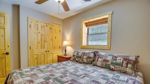 Ein Schlafzimmer mit Holztür, Fenster mit Aussicht, Bett mit Steppdecke und Nachttisch mit Lampe.