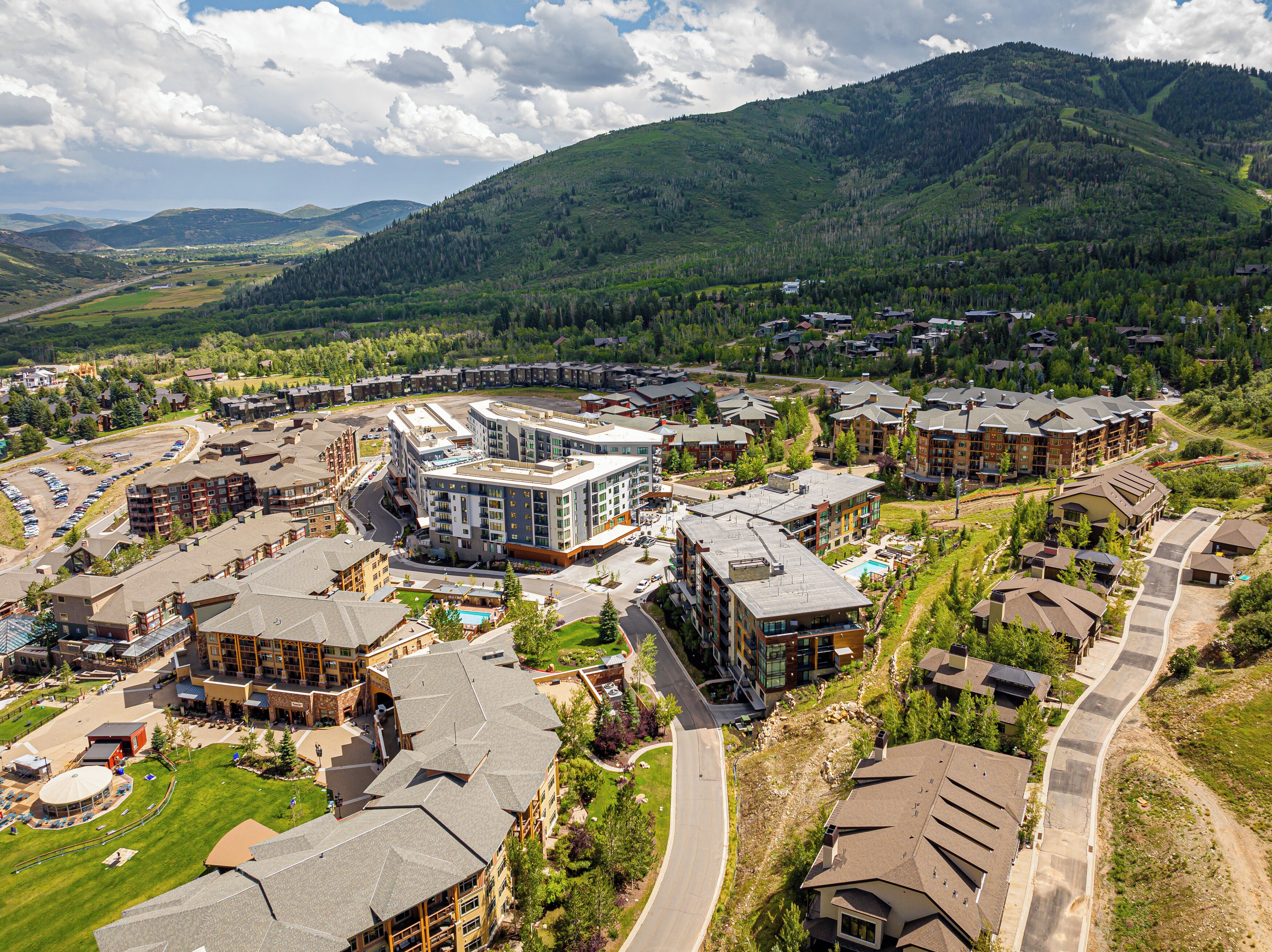 A modern hotel complex with multiple buildings, a central courtyard, and a view of surrounding mountains.