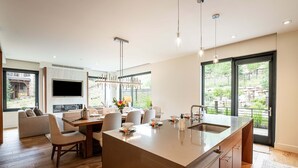 A modern kitchen with a large island, dining area with chairs, a TV mounted on the wall, and large windows offering a view of the outdoors. - Unbeatable Location! Near Hiking Trails! Park City Lift 301 Ski-in/Ski-out (Park City)