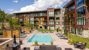 A modern building with a swimming pool, outdoor seating, and a stone wall. - Unbeatable Location! Near Hiking Trails! Park City Lift 301 Ski-in/Ski-out (Park City)