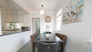 Un coin repas comprenant une table avec un plateau en verre, quatre chaises, une horloge et un tableau accroché au mur.