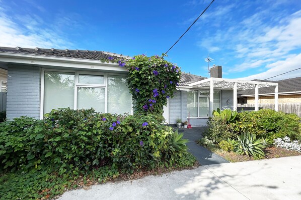 A residential house with a covered porch, a garage, and a well-maintained garden with various plants and flowers.