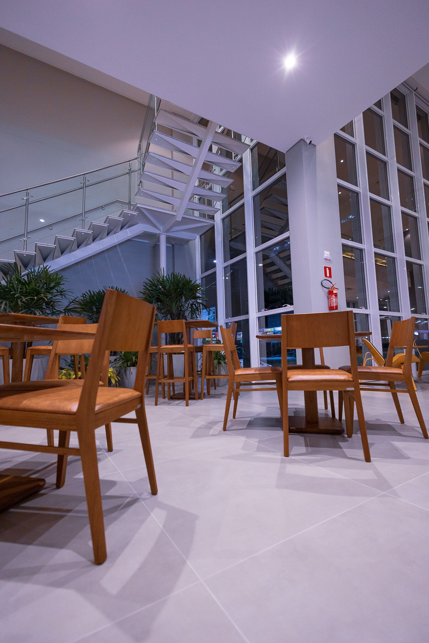Un espace intérieur spacieux, doté de chaises et de tables en bois, de grandes fenêtres et d’un escalier.