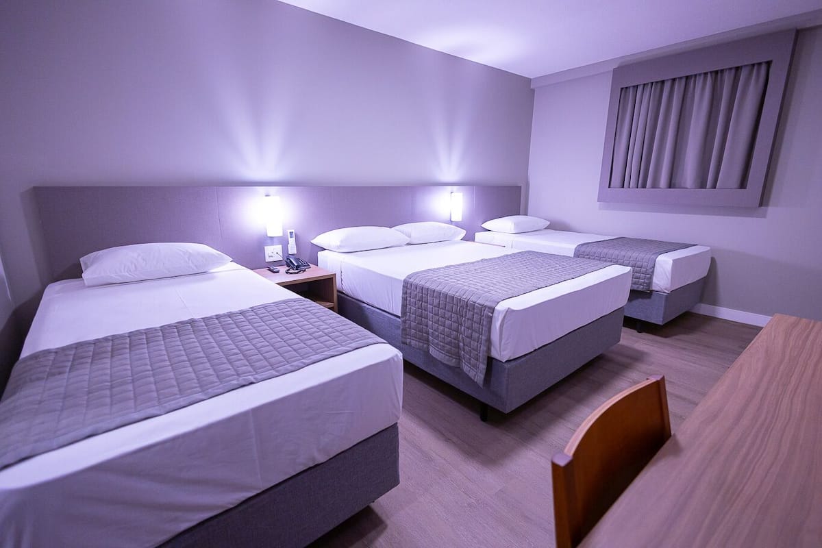 A hotel room with three single beds, a wooden desk, and a nightstand with a phone.