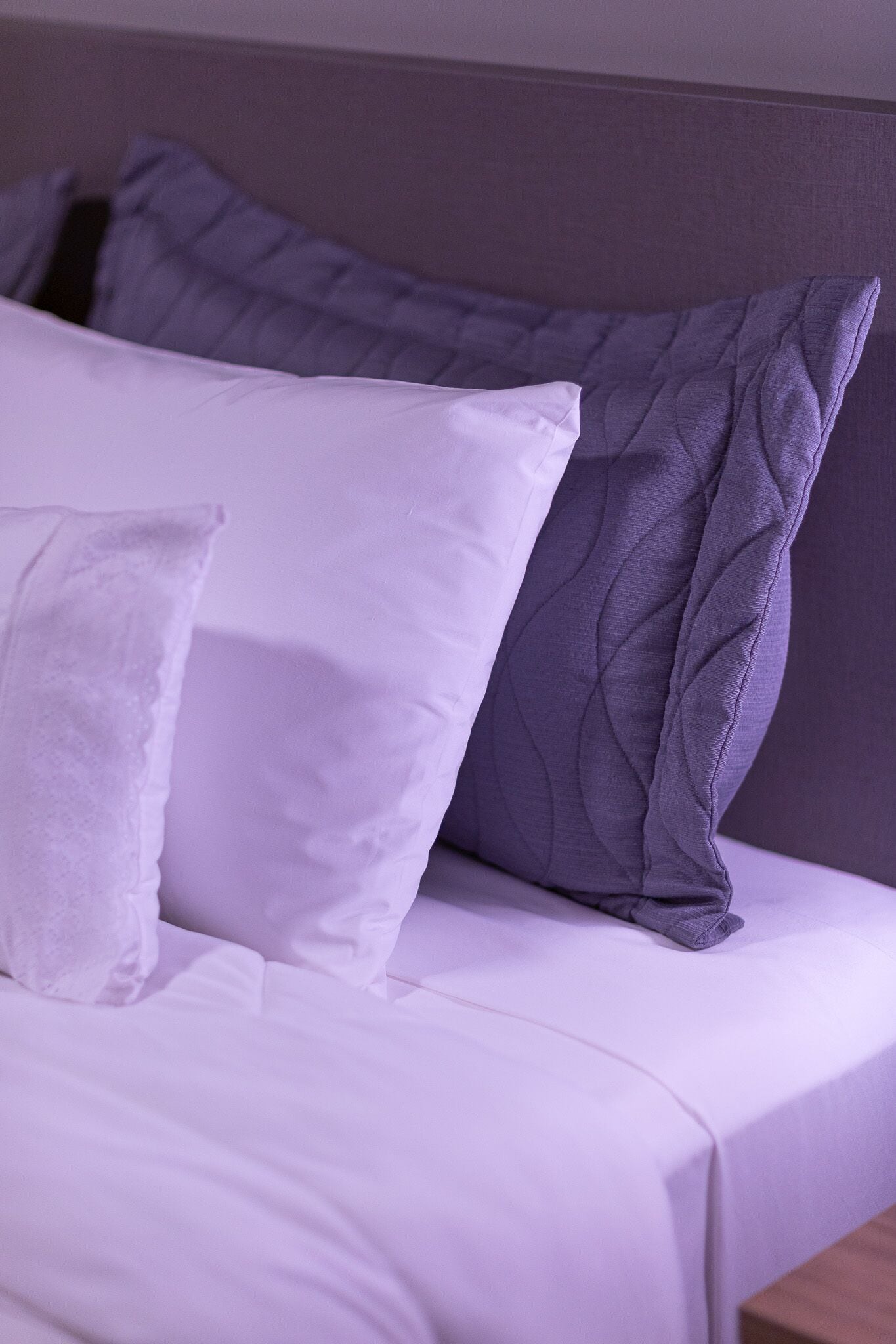 A bed with white bedding and two pillows, one white and one grey.