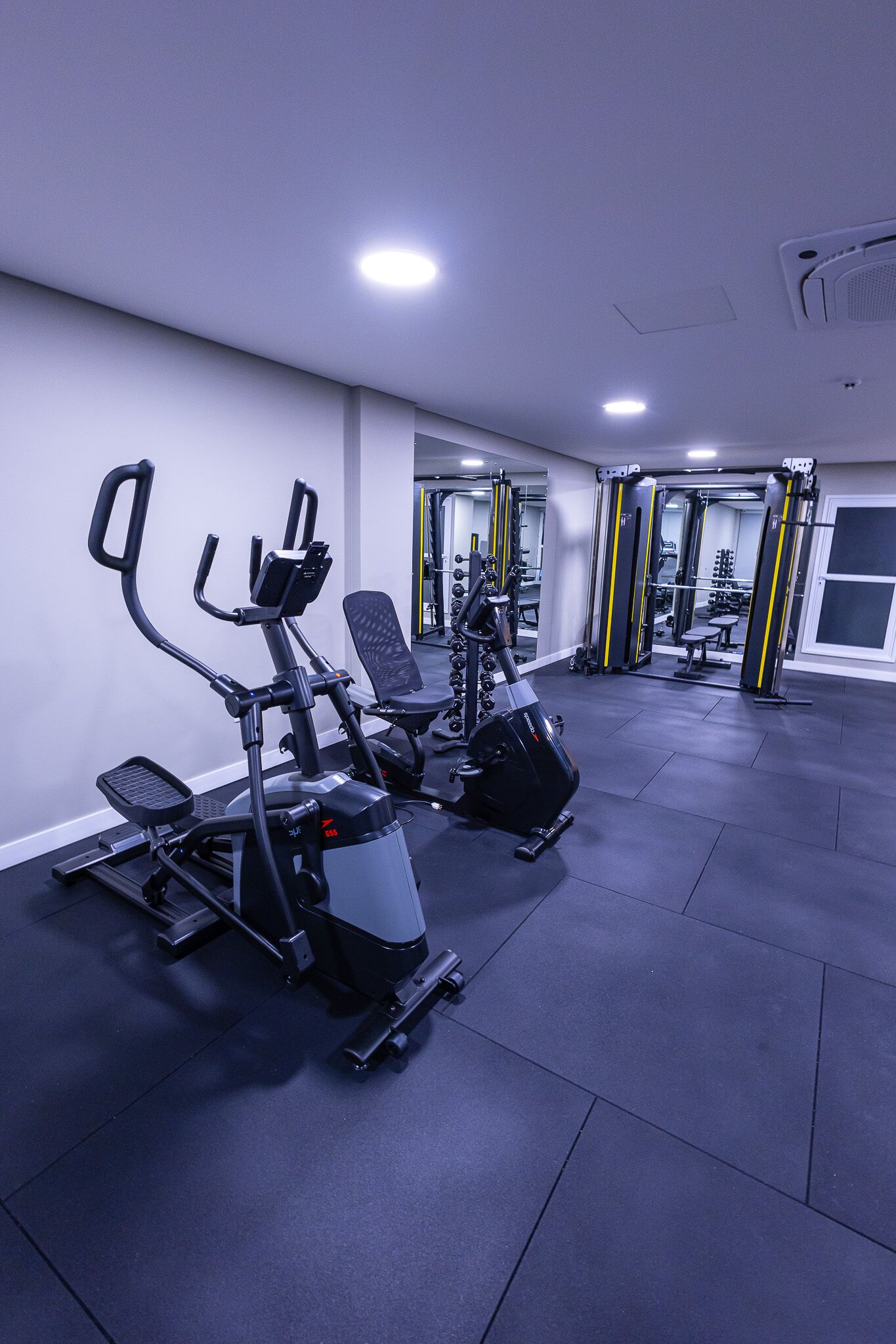 Un gimnasio con equipo de ejercicio, un espejo grande y una puerta que da a otra habitación.