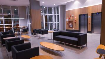 Eine moderne Lobby mit einer schwarzen Couch, Holztischen und schwarzen Stühlen.