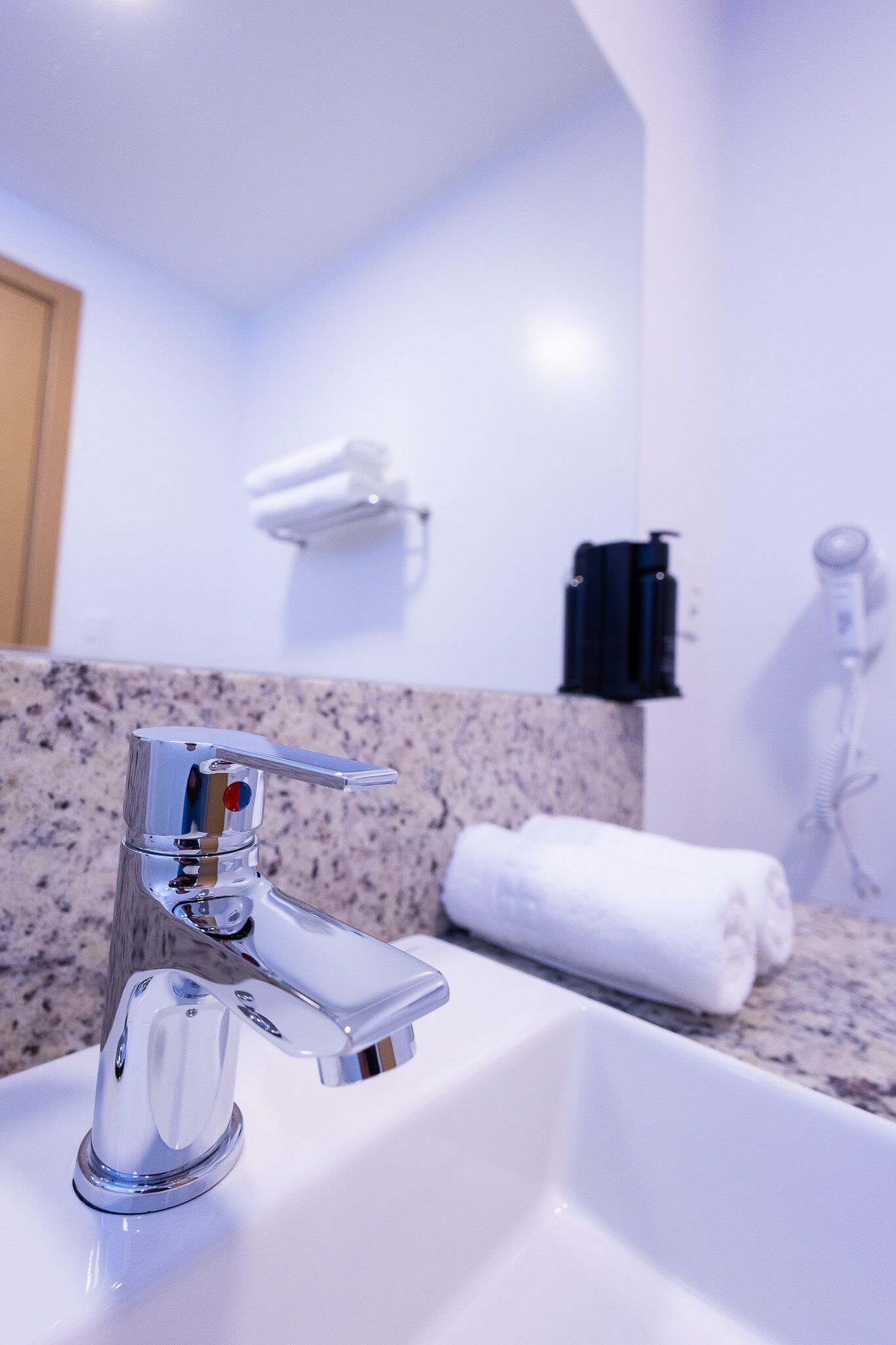 A bathroom with a chrome faucet, a white sink, a towel, and a towel rack.