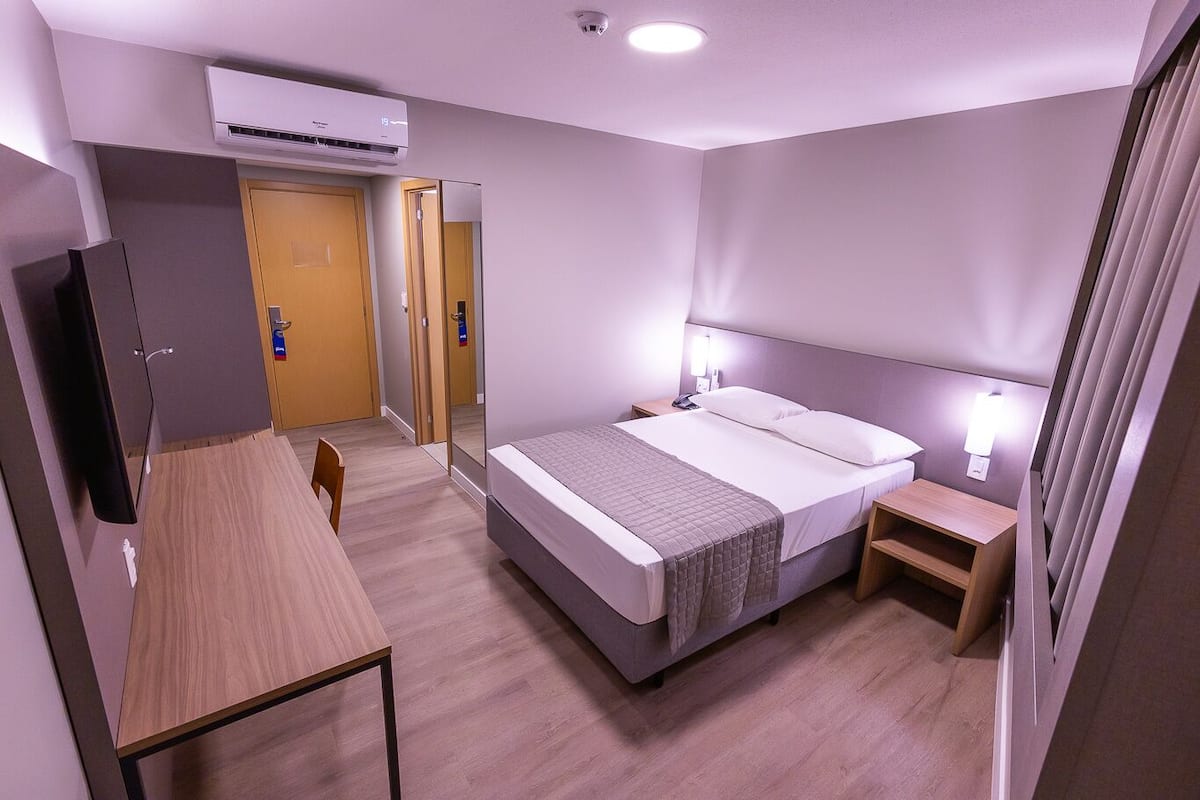 A hotel room with a bed, bedside tables, a desk, and a television.