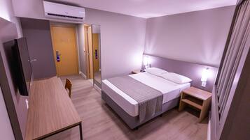 Quarto de hotel com cama, mesas de cabeceira, escrivaninha e televisão.