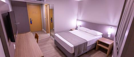 A hotel room with a bed, bedside tables, a desk, and a television.